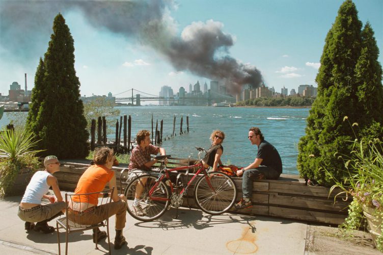 USA. Brooklyn, New York. September 11, 2001. Young people relax during their lunch break along the East River while a huge plume of smoke rises from Lower Manhattan after the attack on the World Trade Center.